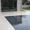 Knife edge swimming pool exactly level with the floating pavers that allow water to pass through the grout joints and be collected below the surface.  